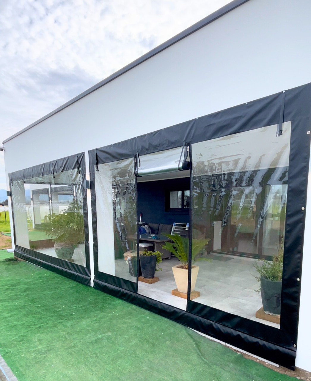 Cierre vertical tradicional de PVC transparente instalado en terraza moderna, con estructura negra y lona semi flexible, ideal para protección contra viento, lluvia y frío sin perder visibilidad exterior.